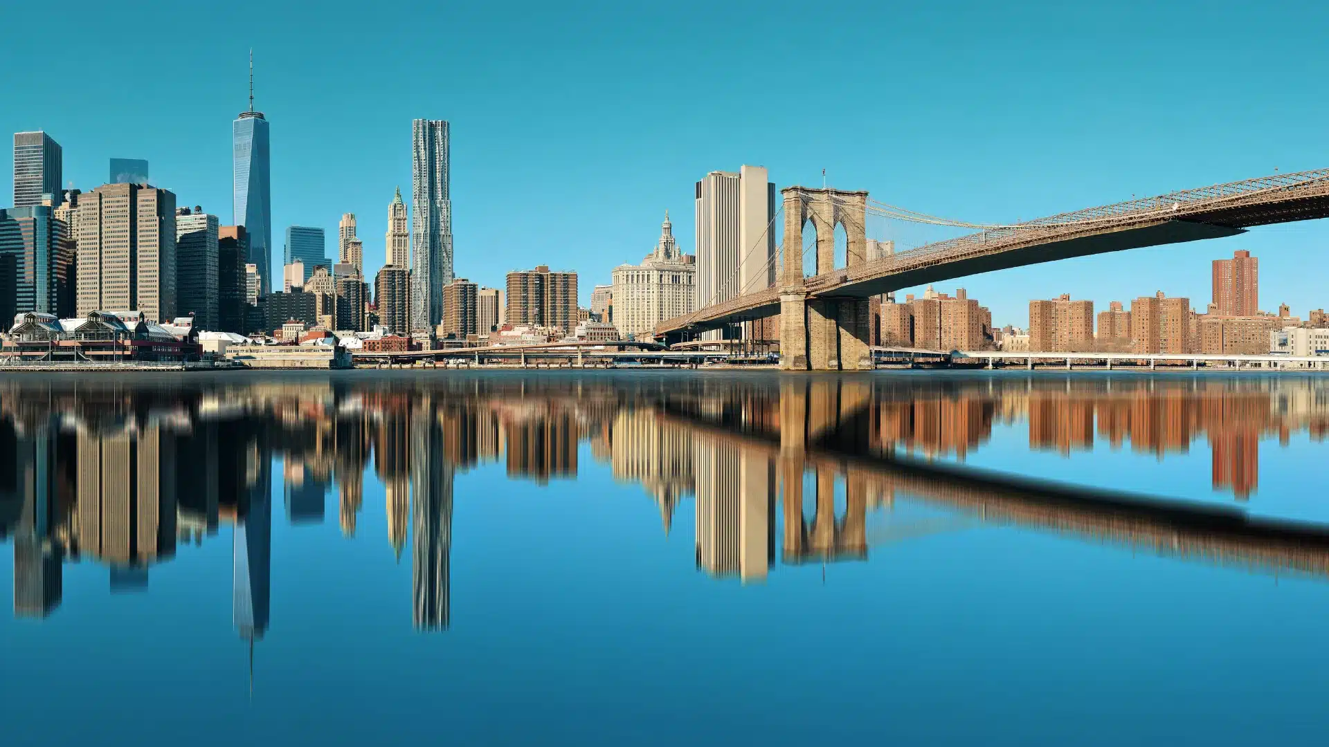 Lower Manhattan skyline reflected on East River with Brooklyn Bridge and downtown New York City skyscrapers