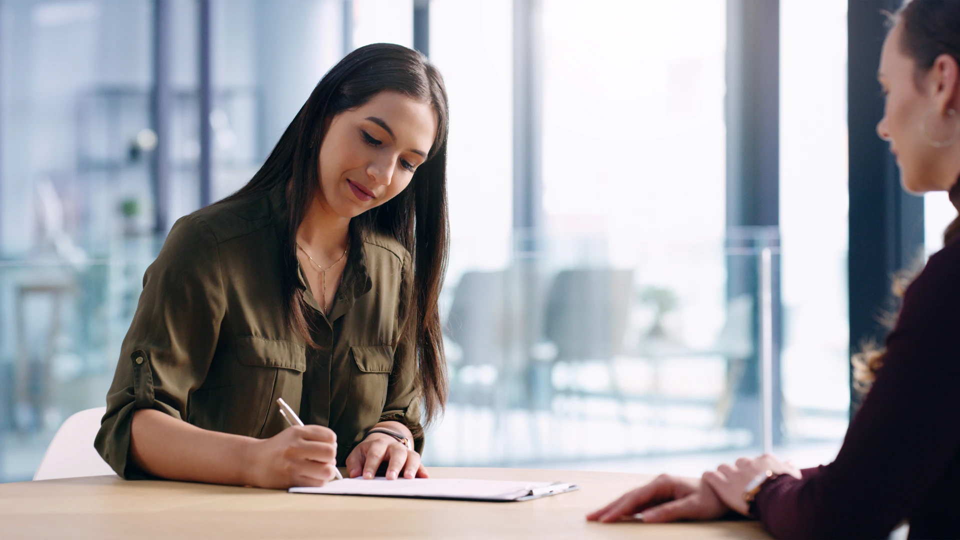 A woman signing a contract while another woman observes, both engaged in a professional discussion.