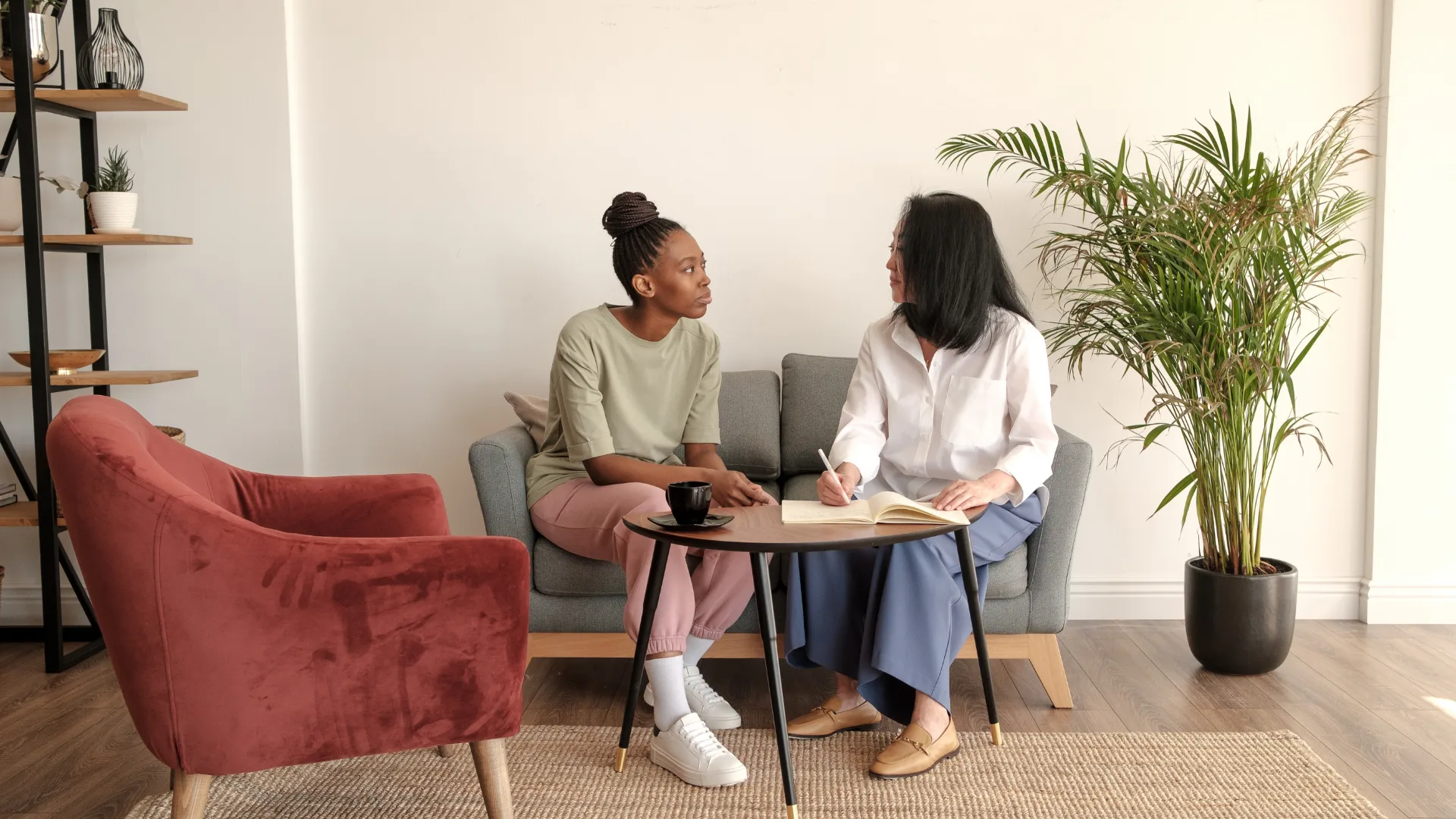 Two women sit together on a couch in a cozy living room, engaged in conversation and enjoying each other's company.