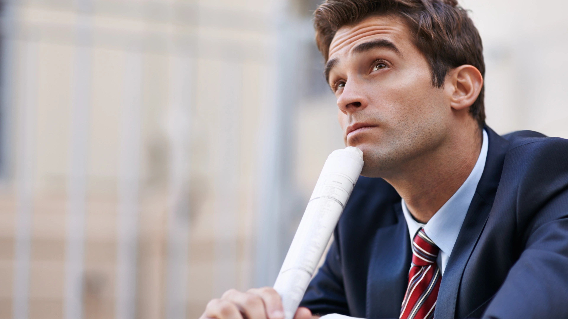 A man in a suit and tie gazes upward, appearing thoughtful or curious about something above him.