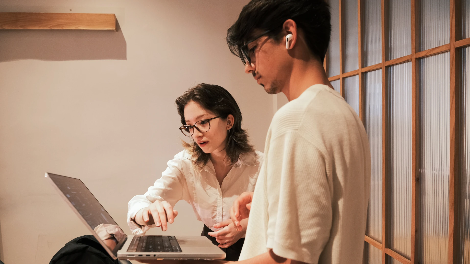 A man and woman collaborate on a laptop, focused on their work in a modern office setting.