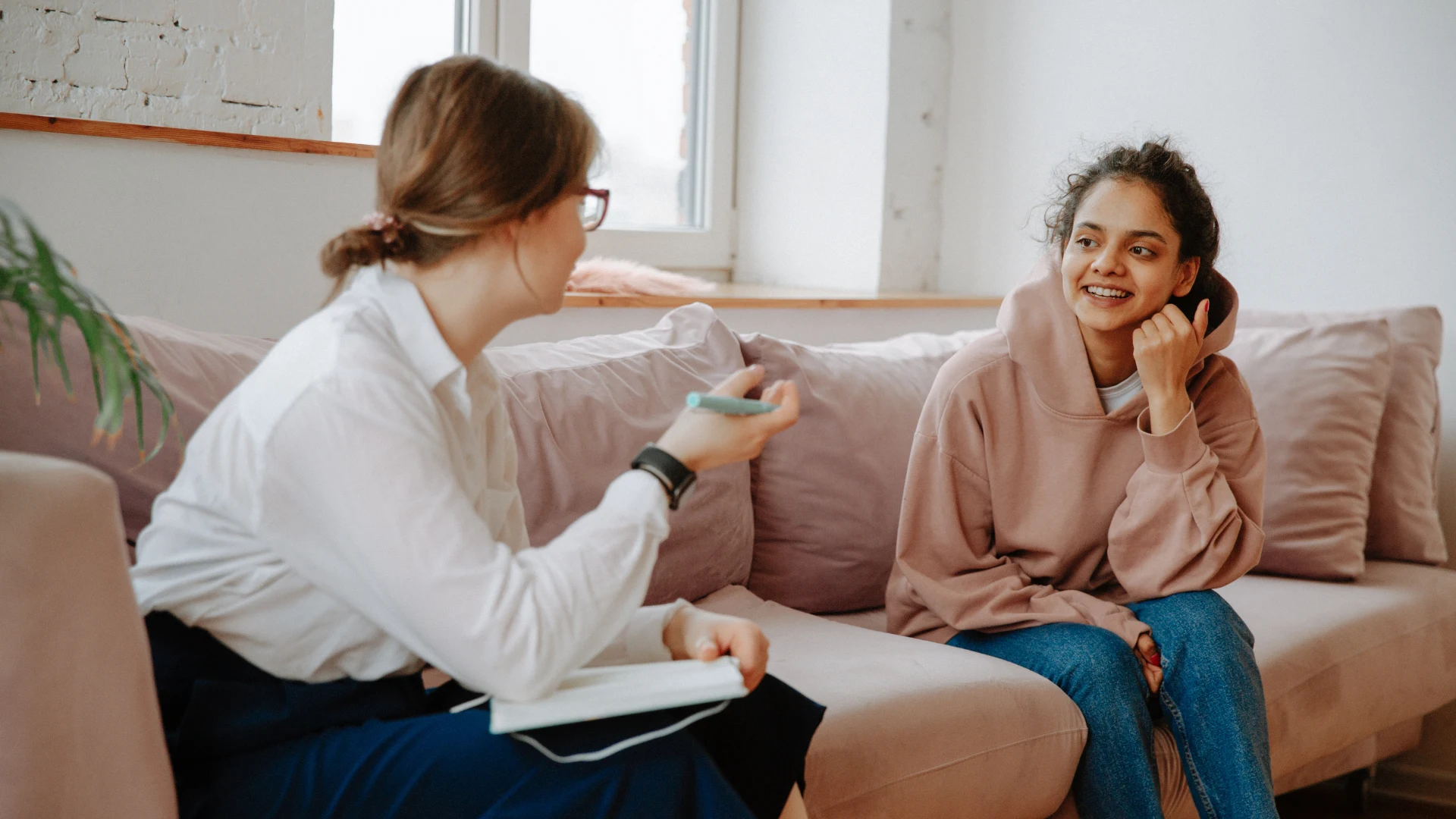 A woman converses with another woman while seated on a couch in a cozy living room setting.