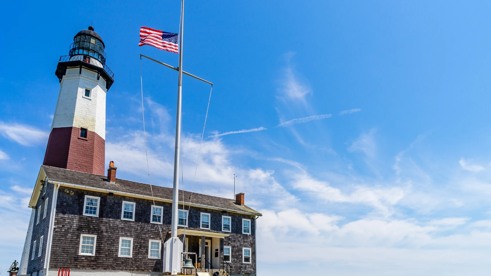 A lighthouse stands tall with a flag waving in front, symbolizing guidance and maritime safety.