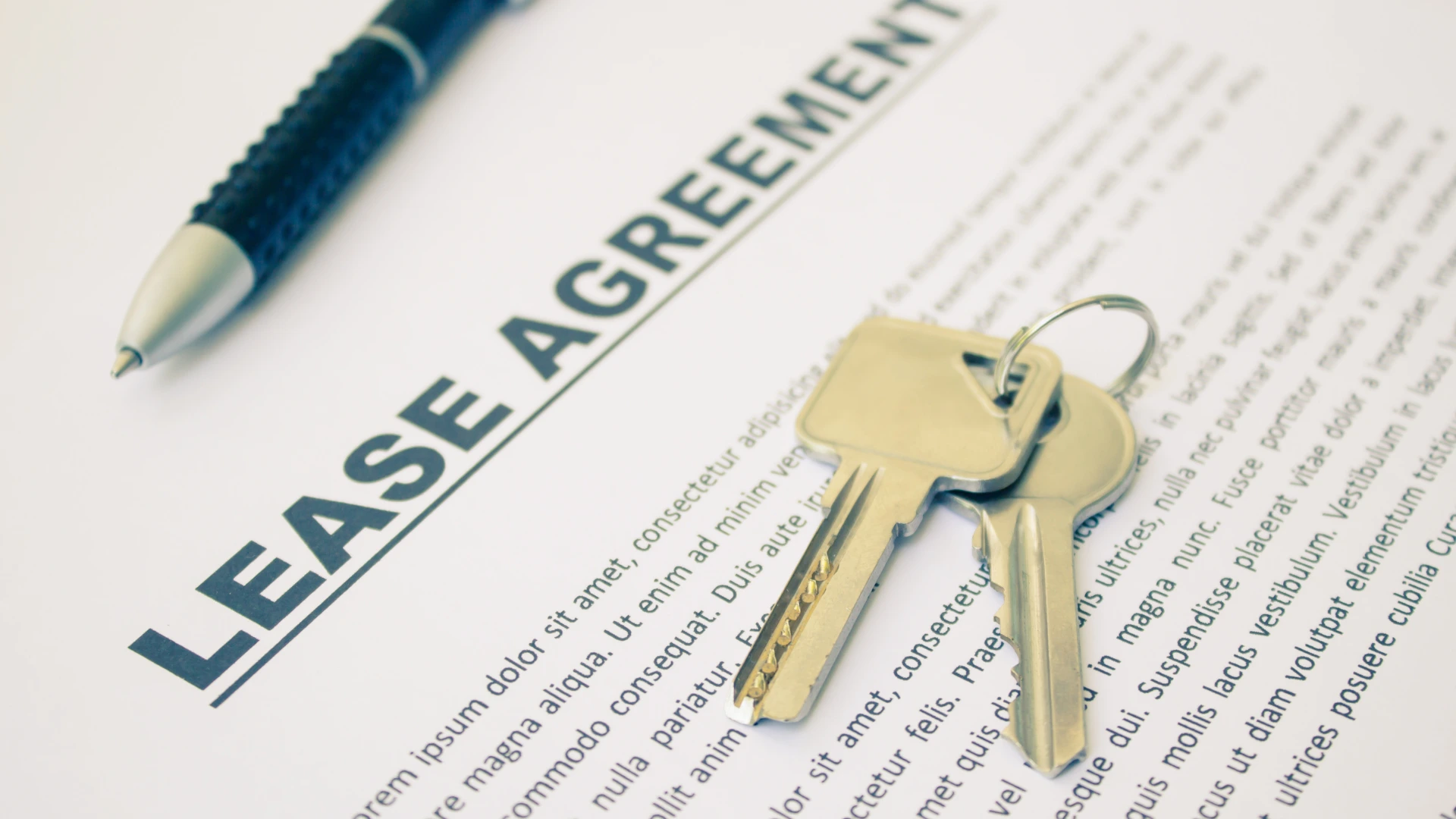 A lease agreement document alongside a set of keys on a wooden surface.