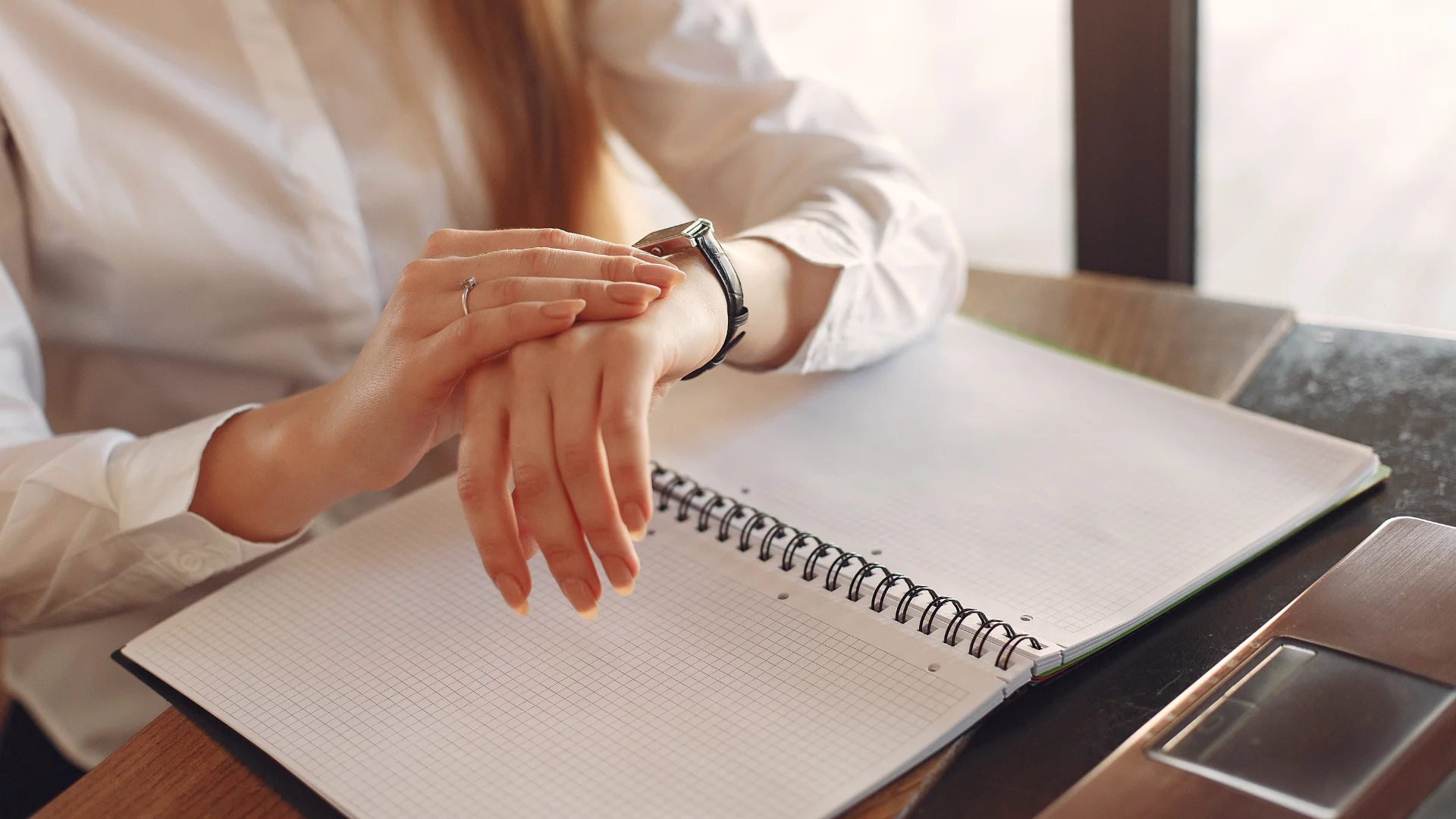 A woman seated at a desk, resting her hands on her wrists, appears contemplative and focused.