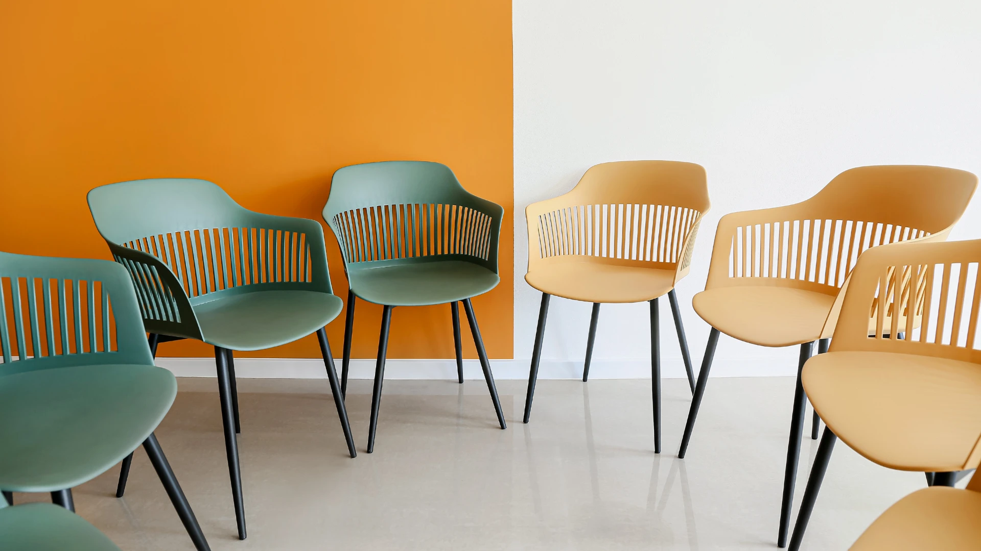 A row of empty chairs positioned against a vibrant orange wall, creating a striking visual contrast.