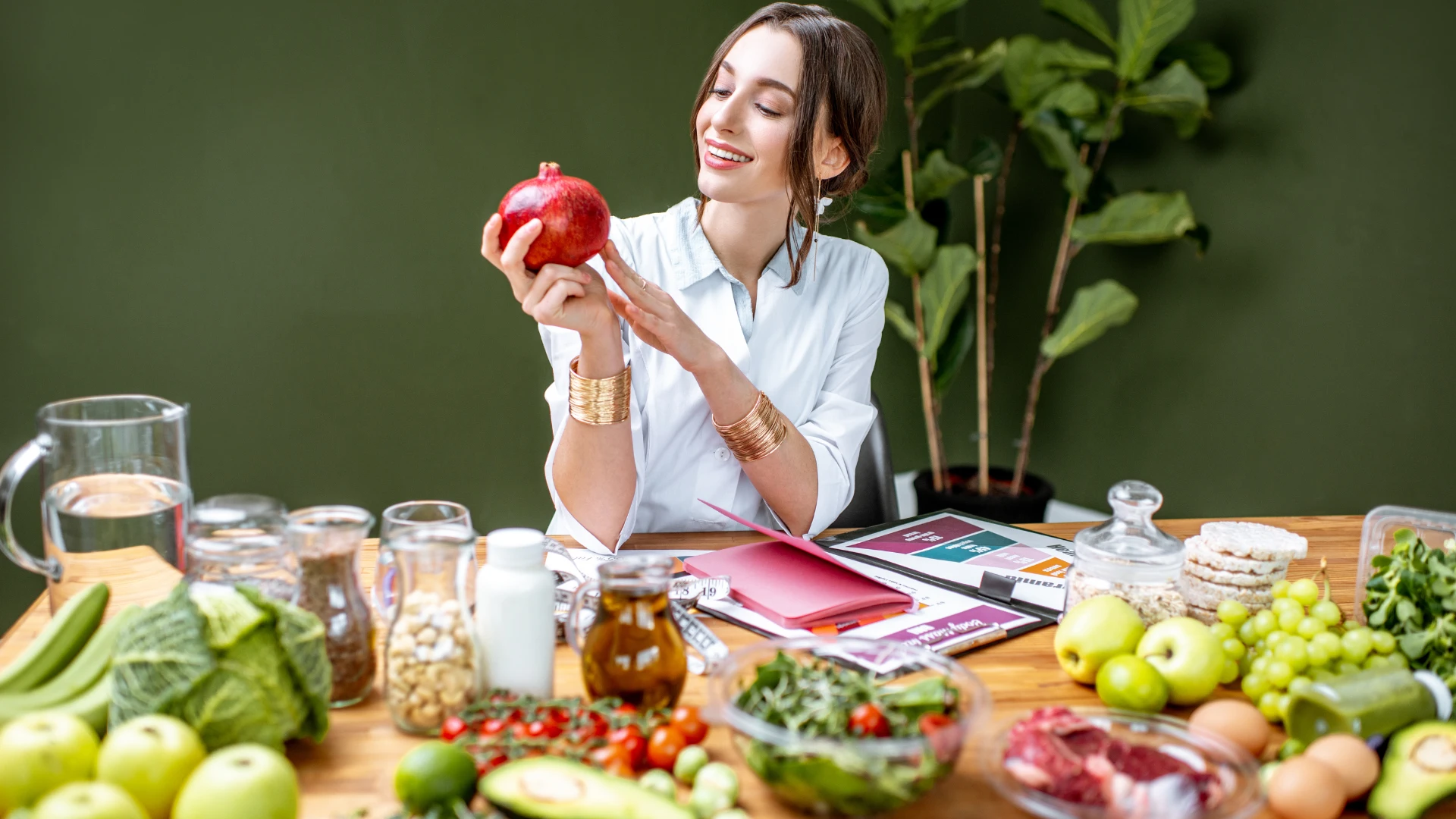 A woman holds an apple in front of a table overflowing with various fruits and vegetables.